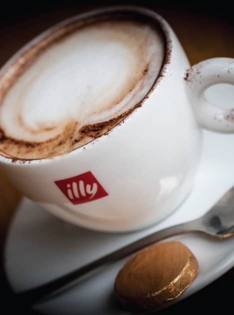 Close-up photograph of a white cup and saucer with Illy coffee in cup and Illy logo on side of cup.