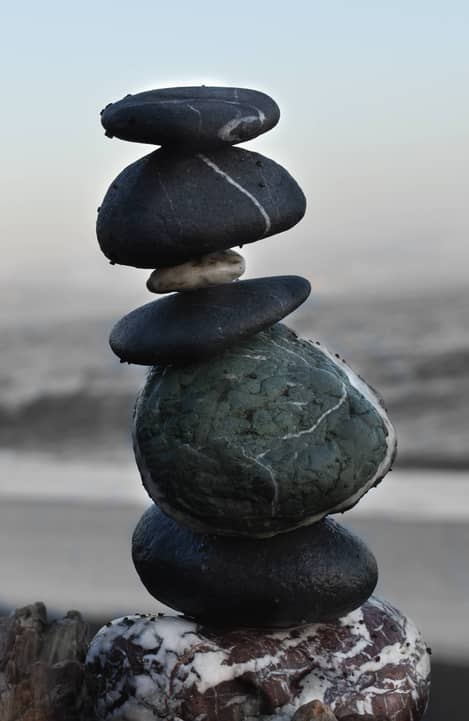 Close-up image of carefully balanced pile of stones on beach with waves breaking in distance.