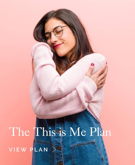 Young woman in pink jumper and denim dress hugging herself