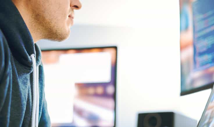 Close up of web developer at a computer screen. Side view of man's face from nose down. Blurred computer screen behind him.