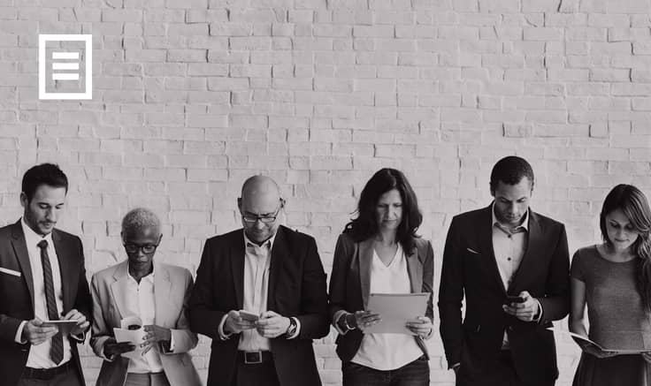 Row of people in suits looking at their phones, with a brick wall behind them.